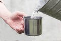 ManÃ¢â¬â¢s hand helds a steel mug and a well water is pouring from a bucket Royalty Free Stock Photo